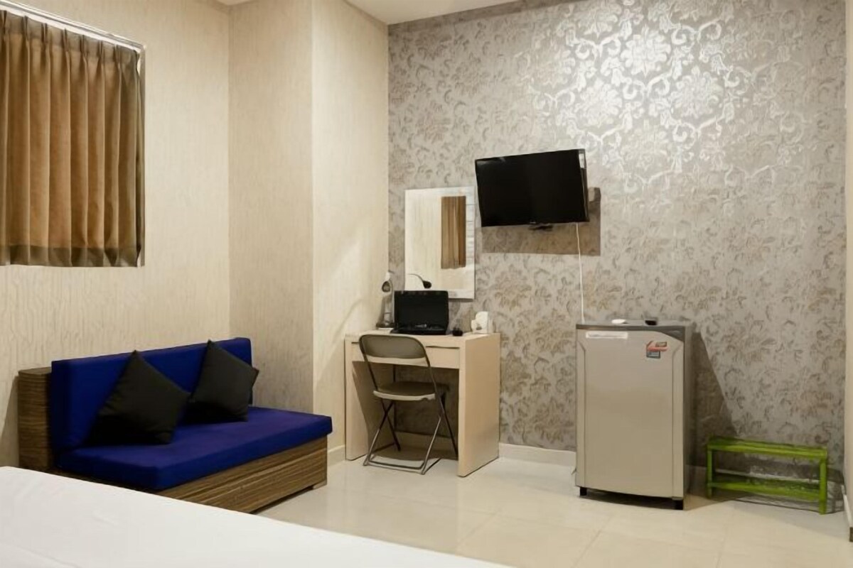 A room with a bed, a blue sofa, a desk with a chair, a television, and a refrigerator.