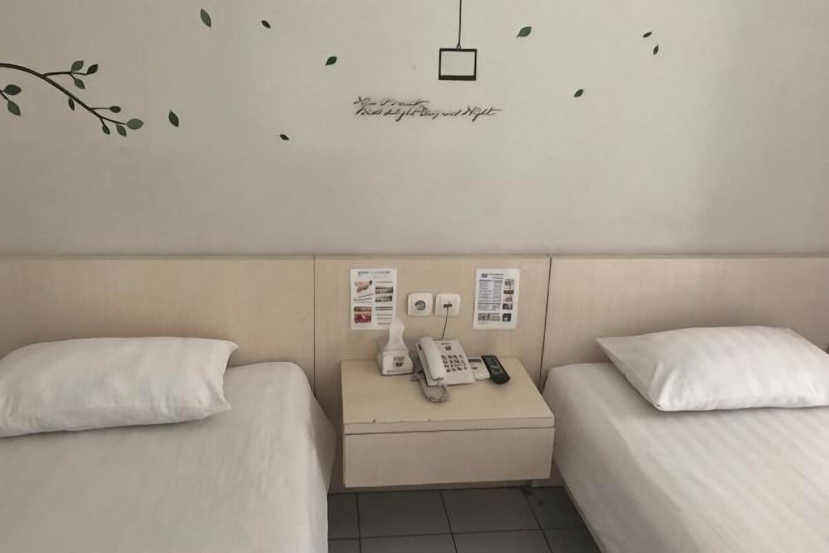 Ein Hotelzimmer mit zwei Einzelbetten, einem Nachttisch mit Telefon und Lampe sowie einer Wanddekoration.