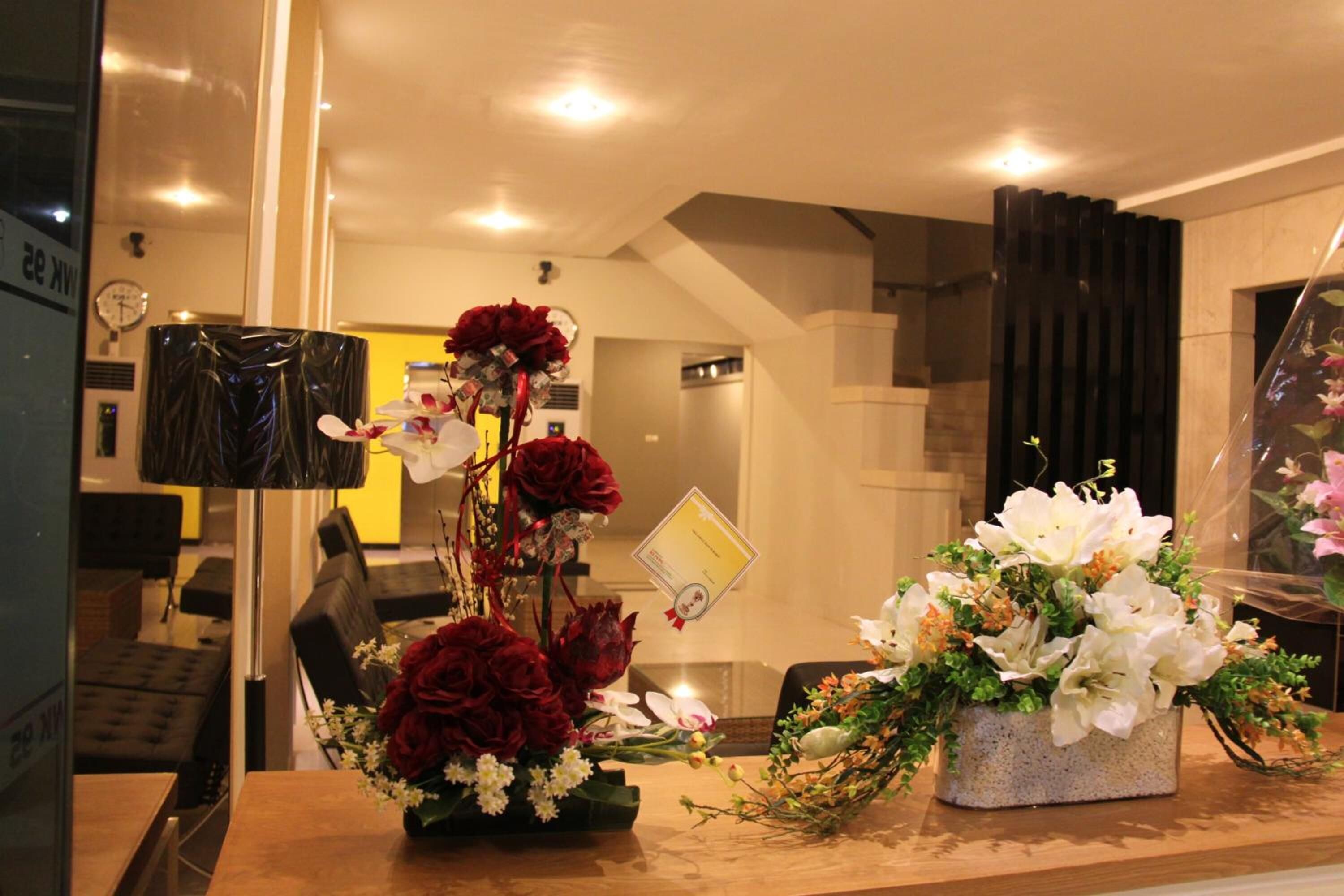 A reception area with a wooden reception desk, two flower arrangements, a clock, and a glimpse of a staircase.