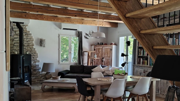 Un vaste espace de vie comprenant un escalier en bois, une cheminée, une table à manger avec des chaises et une bibliothèque.