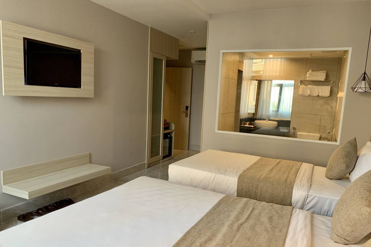 Moderni hotellihuone, jossa on suuri sänky, seinälle asennettu televisio, kylpyhuoneen peili ja pieni oleskelualue.