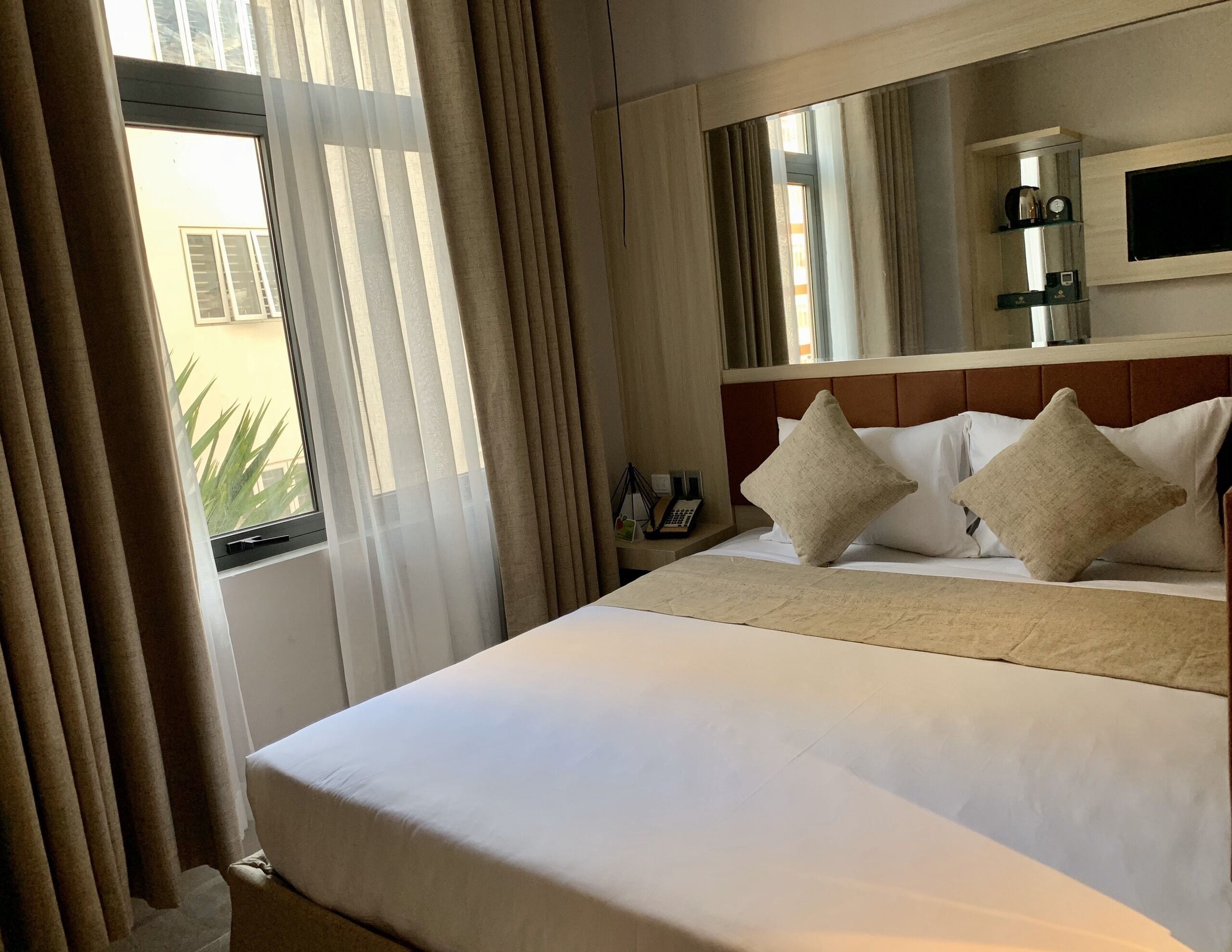 A hotel room with a large bed, a TV mounted on the wall, and a window with curtains.