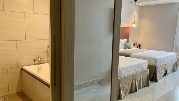 Et moderne hotelværelse med et stort spejl, et badekar, to senge og et lille bord med elkedel.