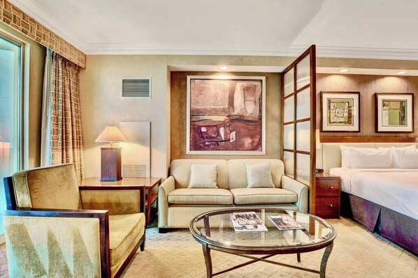 A hotel room with a bed, a sofa, a coffee table, a lamp, and artwork on the walls.