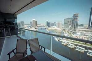 Varanda com duas cadeiras e uma mesa, com vista para um areal marítimo com barcos e edifícios modernos.