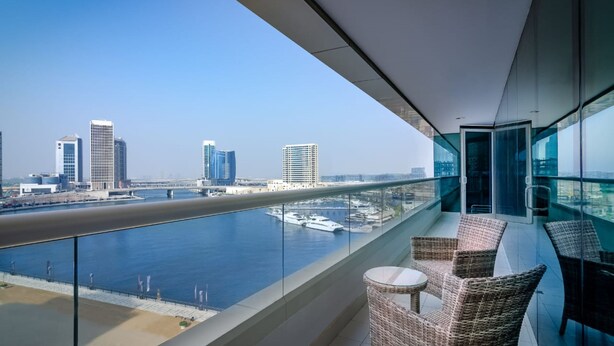 A balcony with wicker furniture overlooking a river and cityscape. - OSKENA Vacation Homes - Damac Maison Canal View  (Dubai)