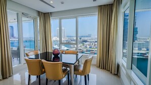 A modern hotel room with a large glass window, a dining table with four chairs, and a decorative vase. - OSKENA Vacation Homes - Damac Maison Canal View  (Dubai)