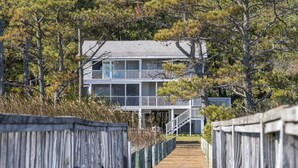 A wooden boardwalk leading to a two-story beachfront house with balconies.