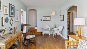 Amplia sala de estar con piso de madera, una mecedora y sillas de mimbre blanco.