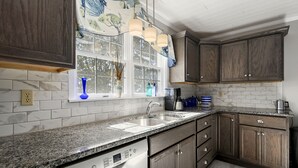 Una cocina con encimera de granito, armarios de madera, lavavajillas Bosch y ventana con vista a árboles.