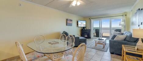 A spacious living room with a glass dining table, wicker chairs, a sofa, and a fireplace.