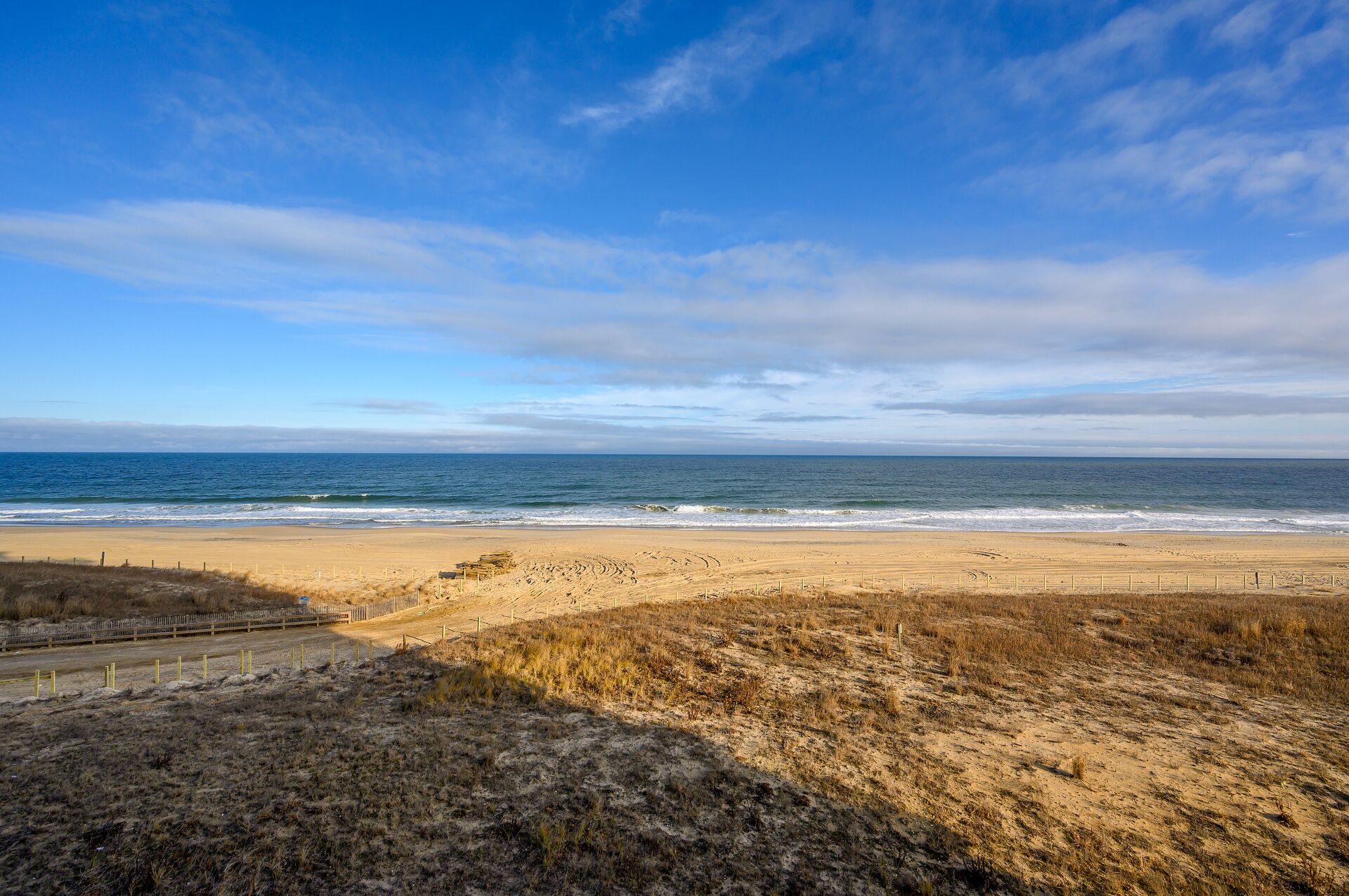 Une plage avec une clôture et de l’herbe sèche au premier plan.