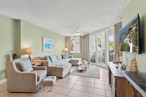 A living room with a sectional sofa, a flat-screen TV, and a view of a house through large sliding glass doors.