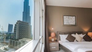 Ein Hotelzimmer mit großem Fenster, einem Bett mit Kissen, einem Nachttisch mit Lampe und einem gerahmten Bild an der Wand.