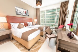 A hotel room with two beds, a desk, a chair, a vase with flowers, and a large window with curtains.