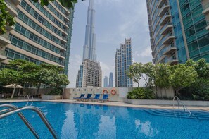 A swimming pool with lounge chairs and a view of tall buildings, including a prominent skyscraper.