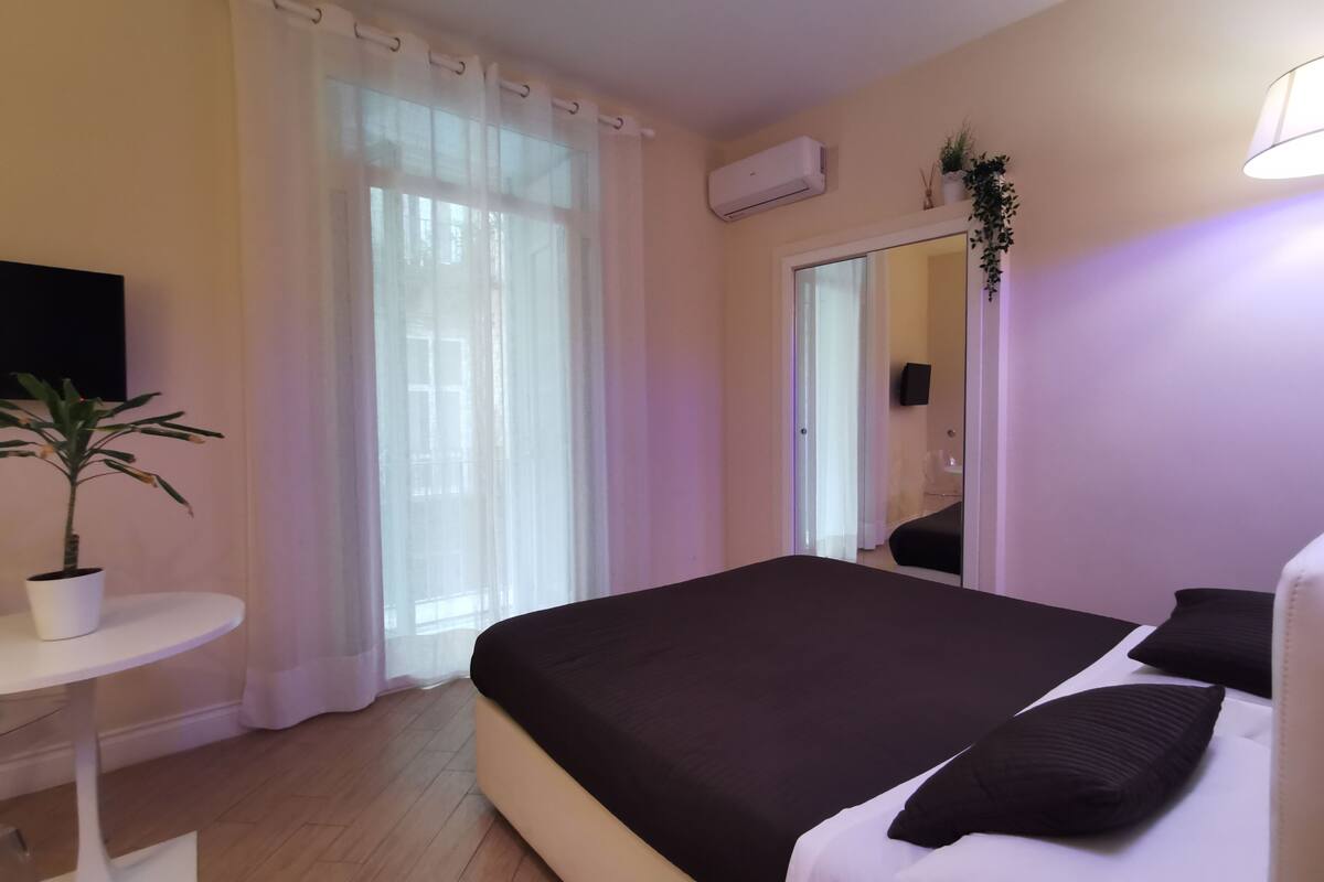 Un dormitorio moderno con una cama grande, una mesita pequeña, una planta en maceta y un aire acondicionado instalado en la pared.