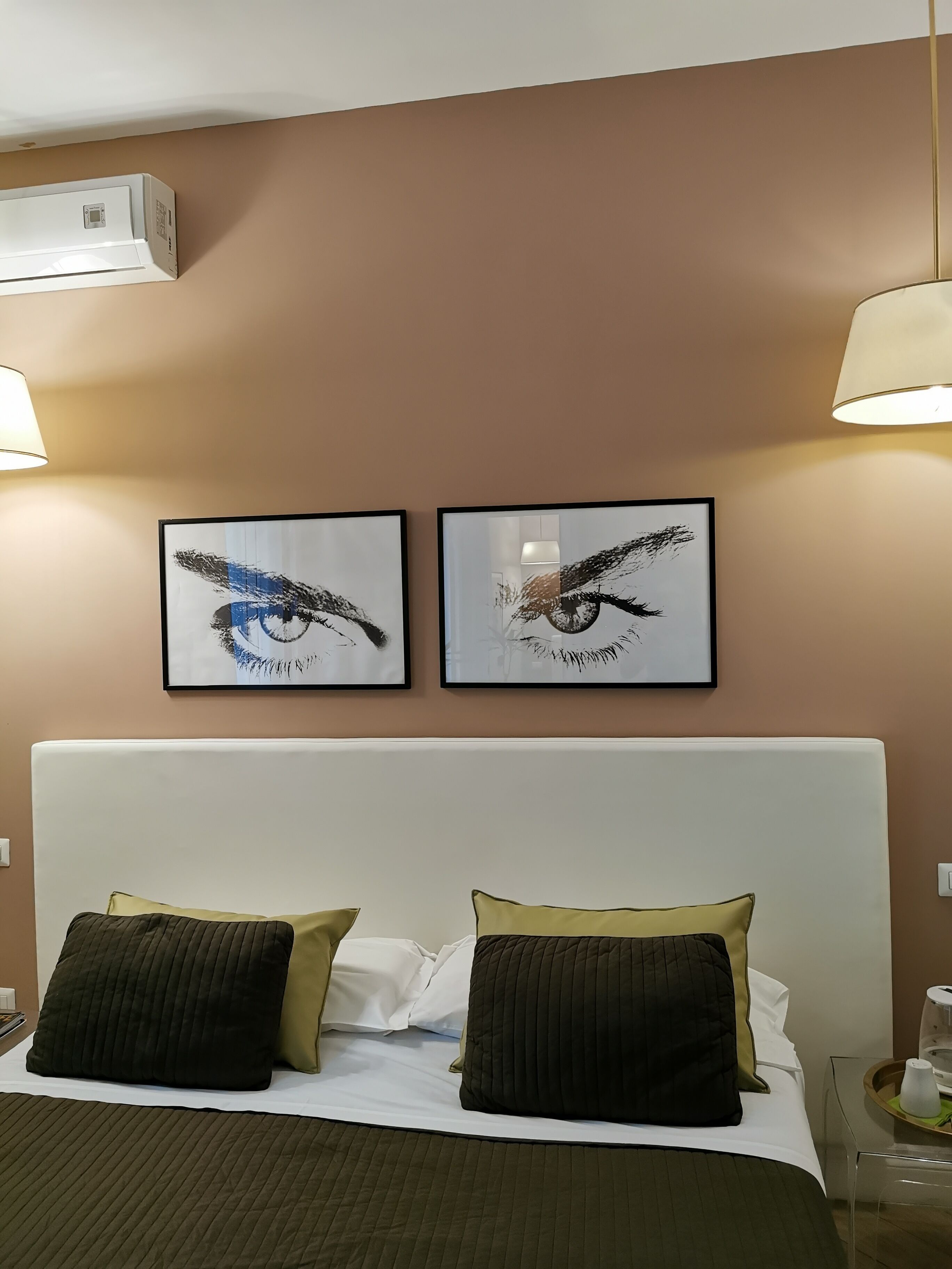 A hotel room with a bed, two framed artworks depicting birds, a white headboard, and a bedside table with a tray.