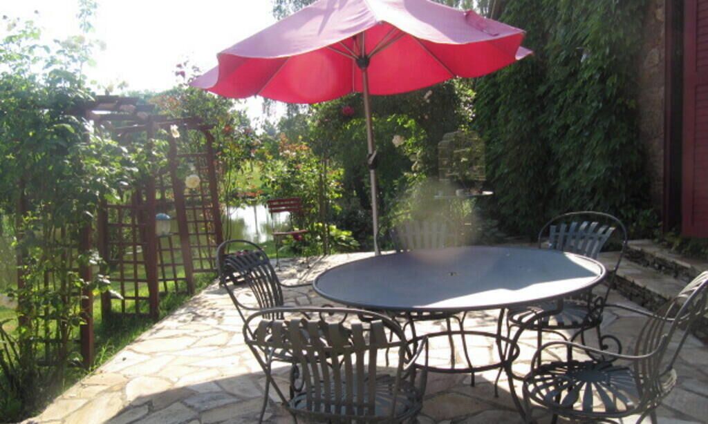 Une terrasse extérieure avec une table ronde et quatre chaises, un parasol rouge et un sol en pierre.