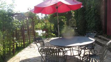 Une terrasse extérieure avec une table ronde et quatre chaises, un parasol rouge et un sol en pierre.