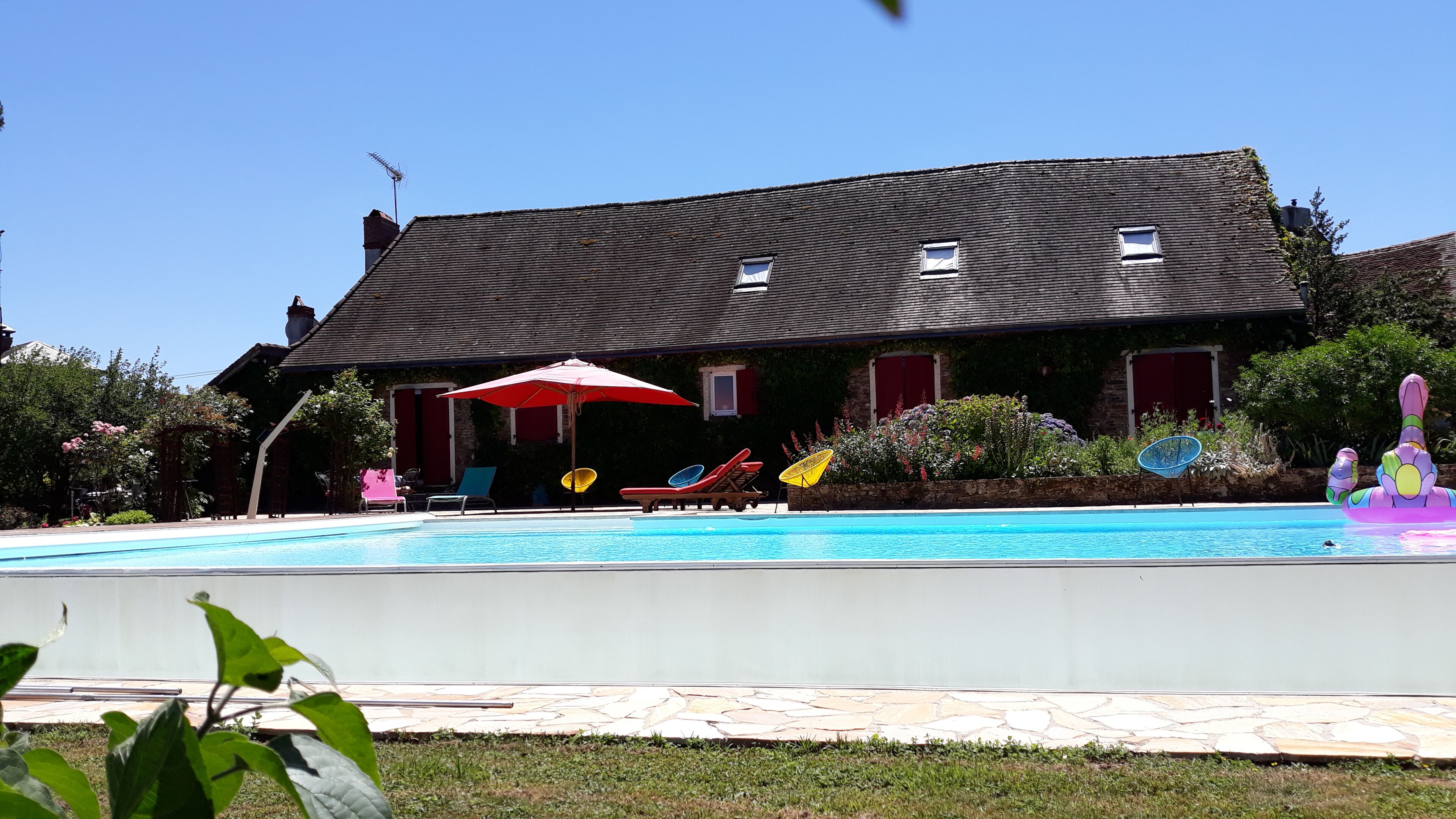 Una casa con piscina, un paraguas rojo y mobiliario de exterior.
