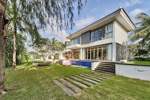 A modern two-story house with a swimming pool, a well-maintained lawn, and a staircase leading to the entrance.