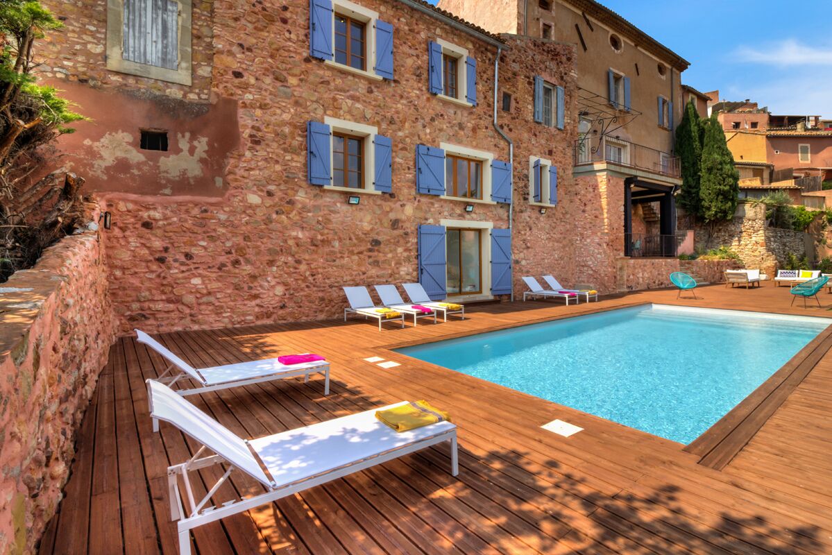 A stone building with a swimming pool, wooden deck, and lounge chairs.