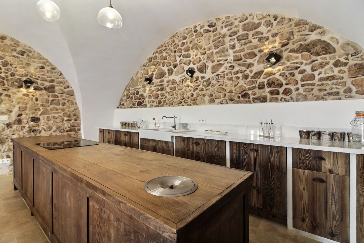 A kitchen with a central island, stone walls, wooden cabinets, and pendant lighting.