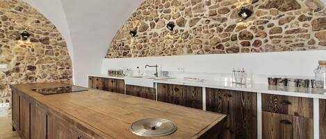 A kitchen with a central island, stone walls, wooden cabinets, and pendant lighting.
