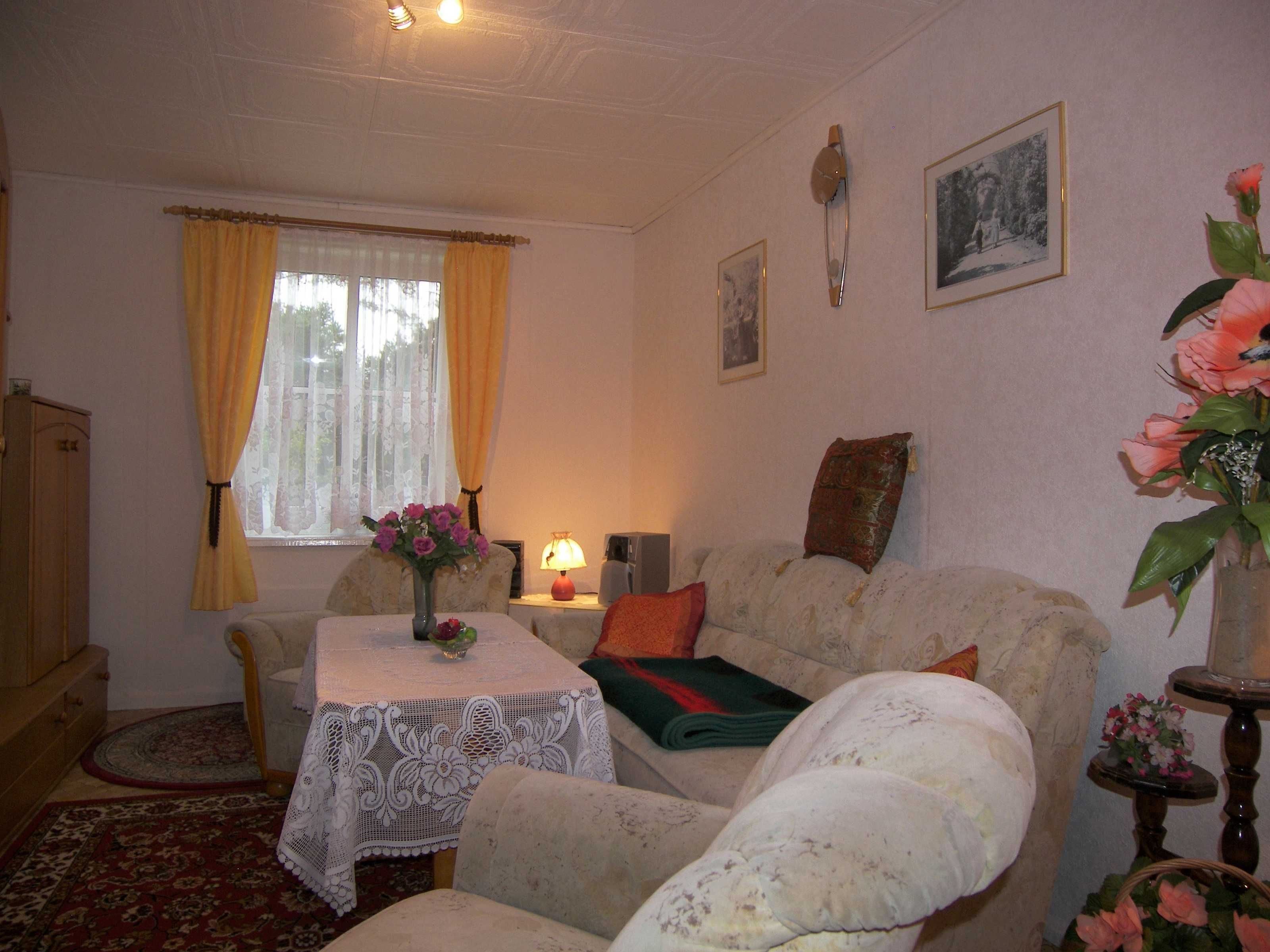 A cozy living room with a sofa, a table with a lace tablecloth, a lamp, and a vase with flowers.