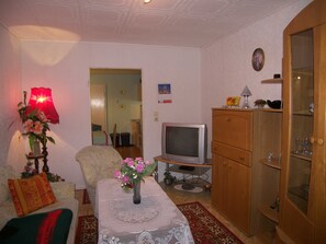 Ein Wohnzimmer mit einer Couch, einem Couchtisch mit Blumenvase, einem Fernseher und einem Schrank.