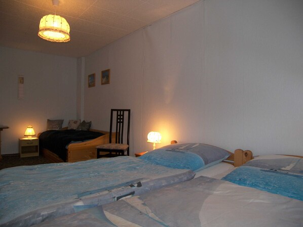 A bedroom with two beds, a chair, a nightstand, and a lamp.