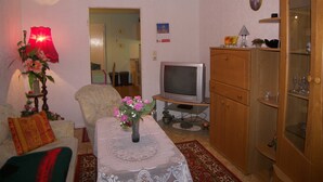 A living room with a sofa, a coffee table with a vase of flowers, a television, and a cabinet. - Bungalow Lange with 2 bedrooms - Bungalow Lange (Heringsdorf)
