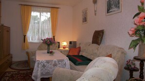 A cozy living room with a sofa, a table with a lace tablecloth, a lamp, and a vase with flowers. - Bungalow Lange with 2 bedrooms - Bungalow Lange (Heringsdorf)