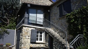 Une maison en pierre dotée d’un balcon, d’un escalier et d’un petit espace extérieur aménagé pour s’asseoir.