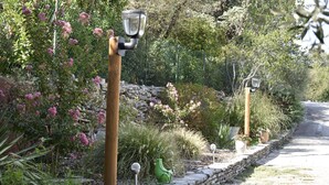 Un chemin de jardin bordé d’un muret en pierre, d’un poteau en bois et d’un lampadaire.