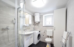Enjoy a refreshing shower in the bathroom, which features a glass-enclosed shower, sink, and compact washing machine.