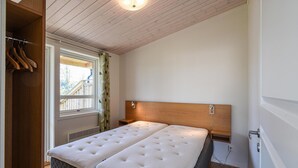Et soveværelse med sengegavl i træ, et vindue med gardiner, en radiator og et garderobeskab med hængende tøj.
