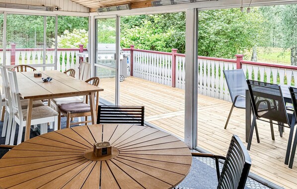 A covered patio with a wooden table and chairs, a grill, and a white picket fence.