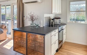 Une cuisine moderne dotée d’un îlot central, d’appareils électroménagers en acier inoxydable et offrant une vue sur l’extérieur.