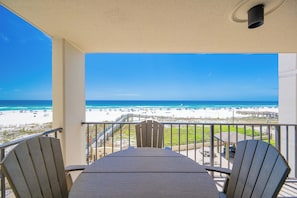 A balcony with a view of the beach, a table, and two chairs.