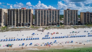A beachfront hotel with multiple high-rise buildings, a sandy beach, and numerous umbrellas.
