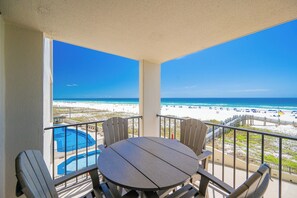 Un balcón con vista a la playa, una piscina y mobiliario exterior.