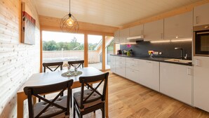 A modern kitchen with wooden cabinets, a dining table with chairs, and a view of the outdoors. - Rosenhaus in Schwarzenberg (Schwarzenberg)