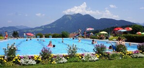 A swimming pool surrounded by colorful flowers and umbrellas, with mountains in the background. - Rosenhaus in Schwarzenberg (Schwarzenberg)