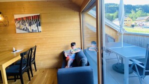 A cozy room with wooden walls, a dining table with chairs, a sofa, and a large window offering a view of a residential area. - Rosenhaus in Schwarzenberg (Schwarzenberg)