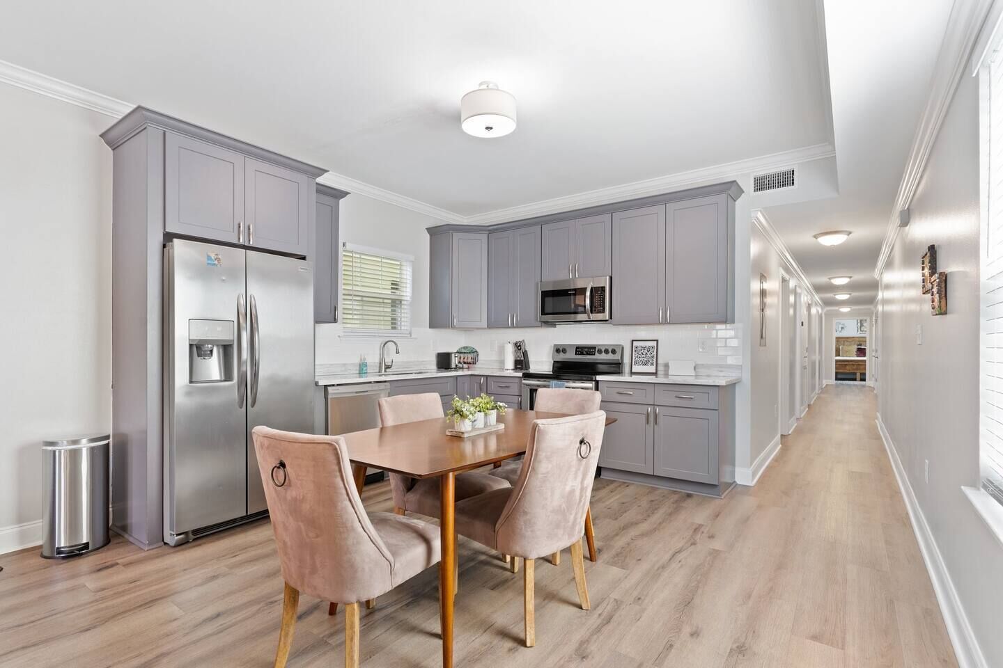 A modern kitchen with grey cabinets, stainless steel appliances, and a wooden dining table with four chairs.