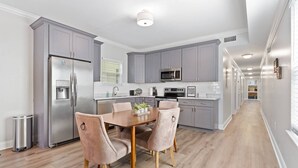 A modern kitchen with grey cabinets, stainless steel appliances, and a wooden dining table with four chairs. - Modern 4BR Mid-City home with heated pool & parking. Steps to streetcar, near FQ & parades. (New Orleans)