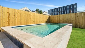 A rectangular swimming pool with a tiled edge, surrounded by a wooden fence and a grassy lawn. - Modern 4BR Mid-City home with heated pool & parking. Steps to streetcar, near FQ & parades. (New Orleans)