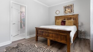 A bedroom with a wooden bed, a ceiling fan, a framed picture, and a leopard print rug. - Modern 4BR Mid-City home with heated pool & parking. Steps to streetcar, near FQ & parades. (New Orleans)